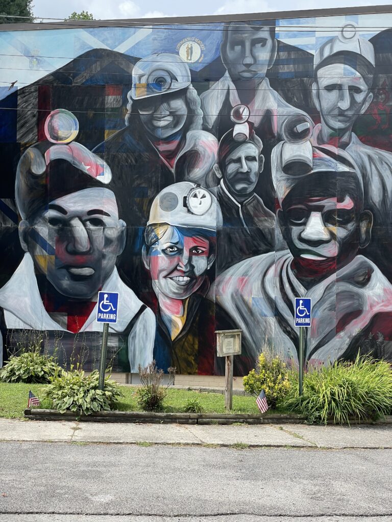 Lacy Hale, Unsung Heroes Mural, Hemphill, KY 2023 Celebrating and Honoring the 31 nationalities of immigrants who came to the mountains of eastern Kentucky to mine coal and were counted on the 1920 census. The underpainting contains all the flags of those nations plus the Kentucky flag.